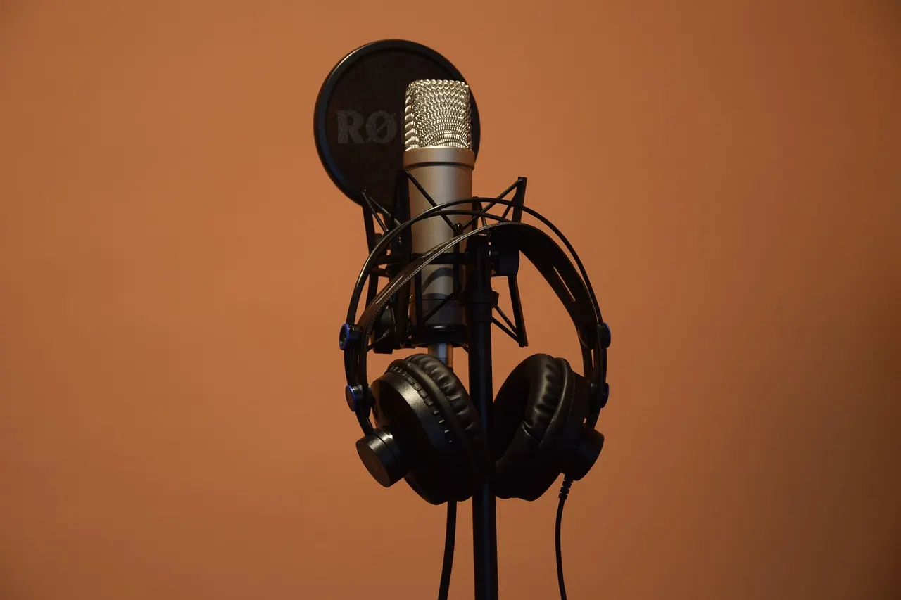 Micrófono de estudio con audífonos colgados sobre un fondo cálido
