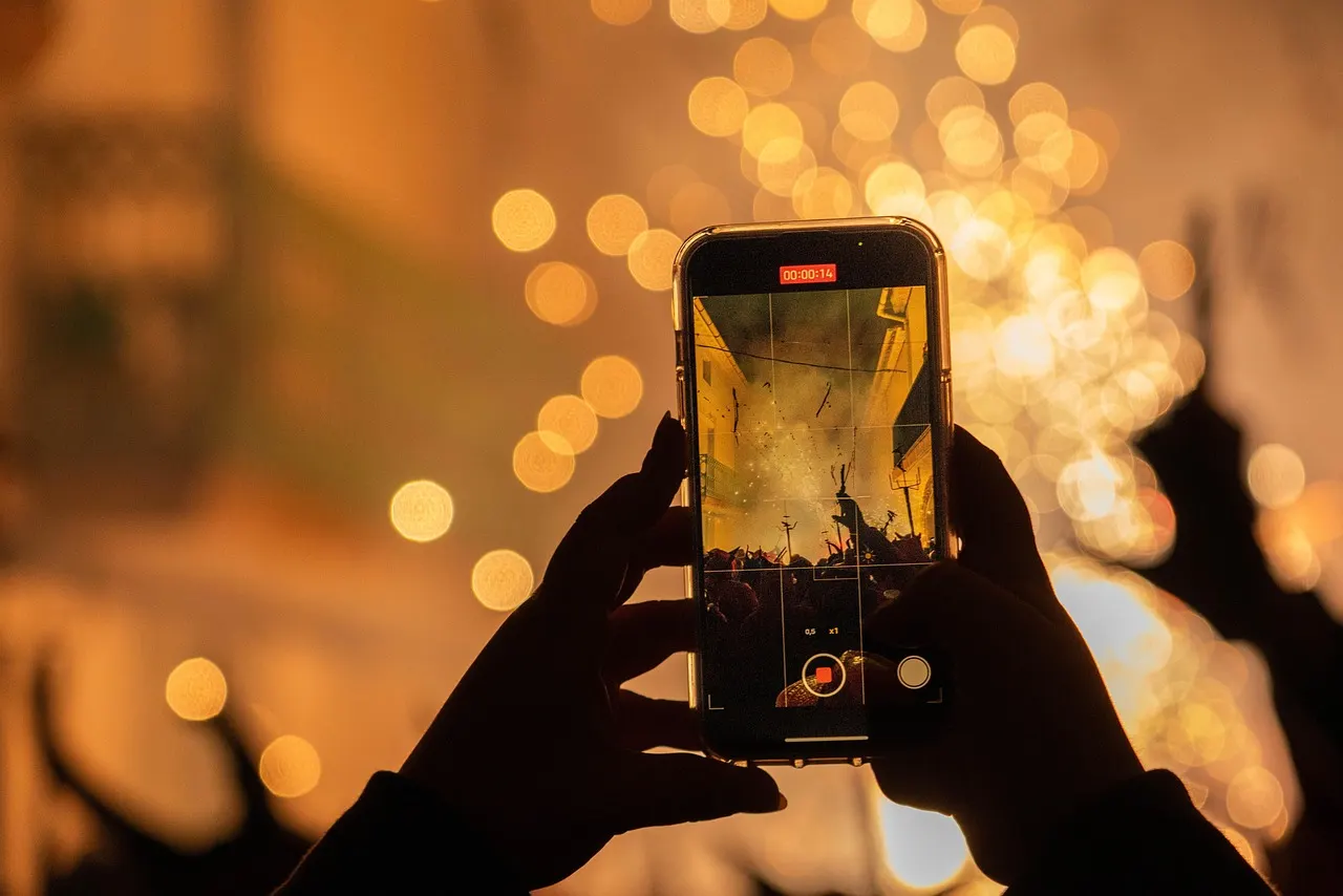 Manos sosteniendo un celular de noche frente a luces desenfocadas