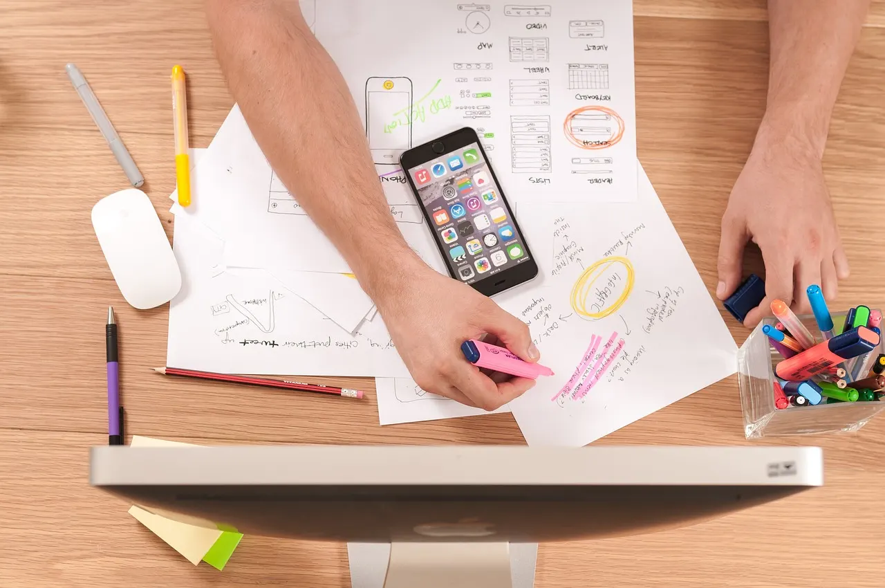 Diseñadora dibujando bocetos de interfaz junto a un celular y marcadores