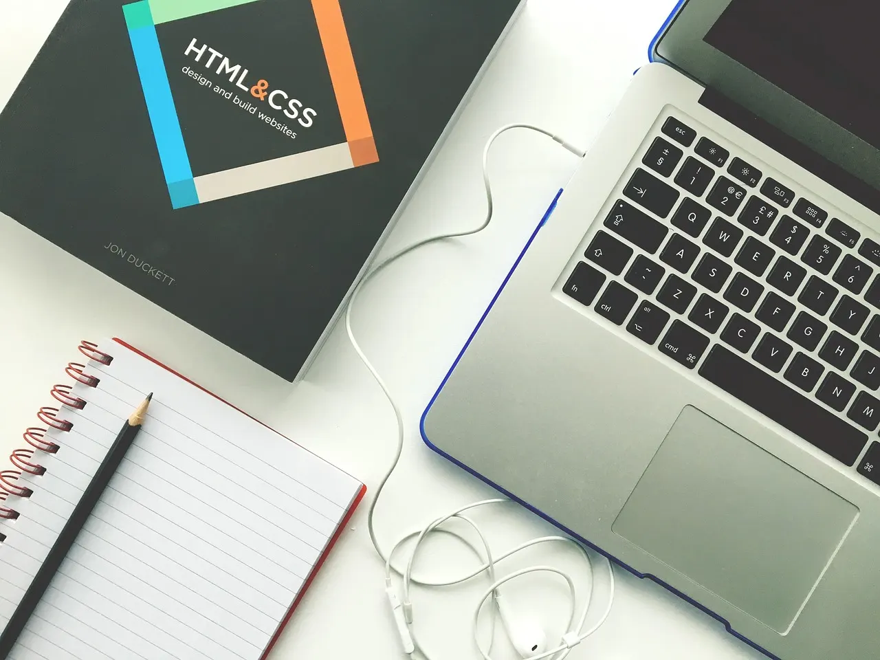 Portátil junto a un libro de HTML y CSS sobre un escritorio